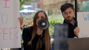 Woman and man with speaker and signs, protesting for catheter coverage