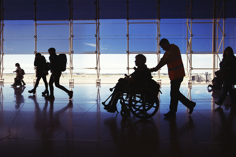Silhouette of man in wheelchair and people carrying luggage and walking in airport