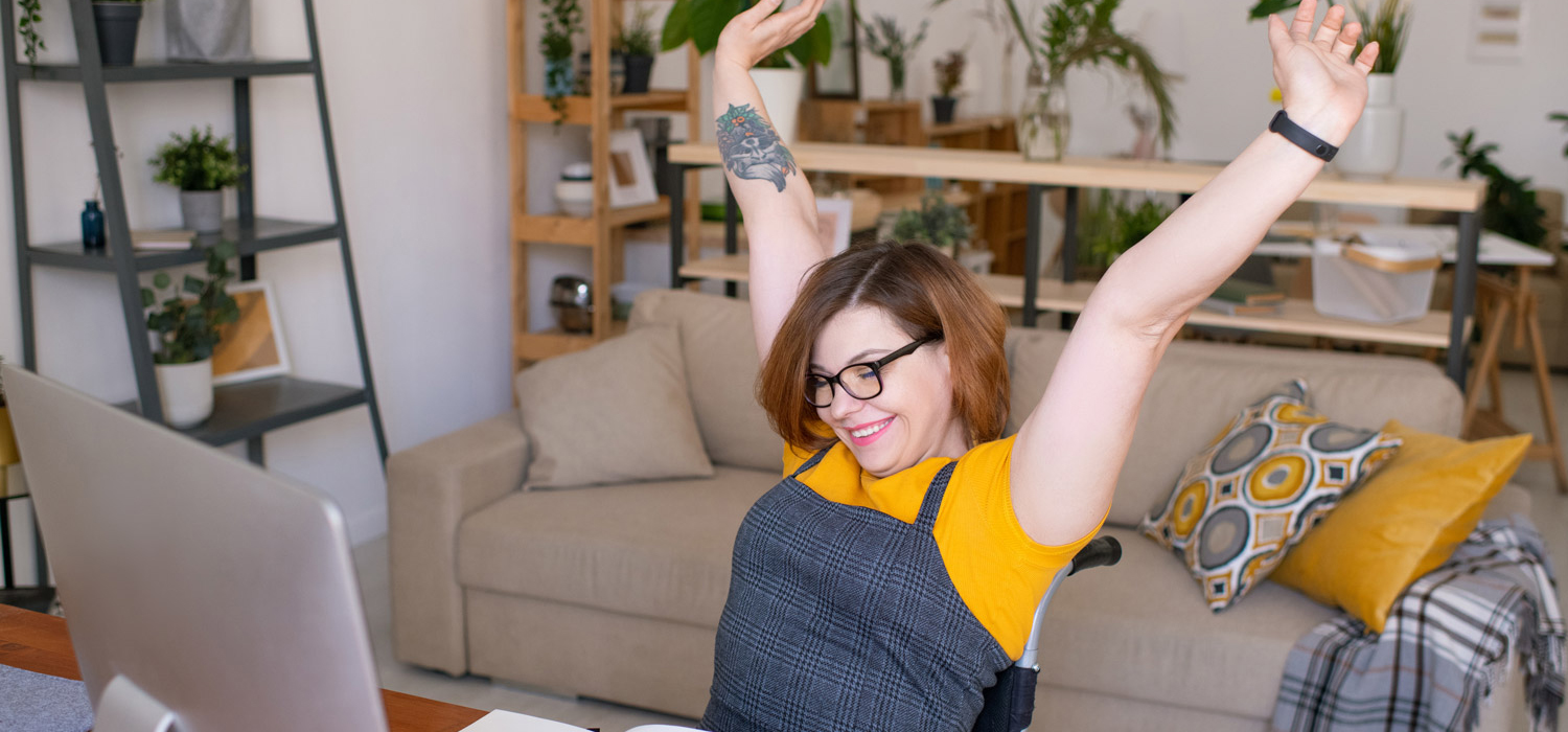 A woman at a computer cheering with her arms in the air
