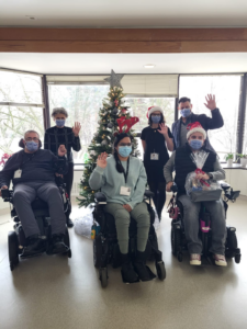 Group of staff and community members at Lyndhurst, waving in santa hats beside Christmas tree with gift baskets