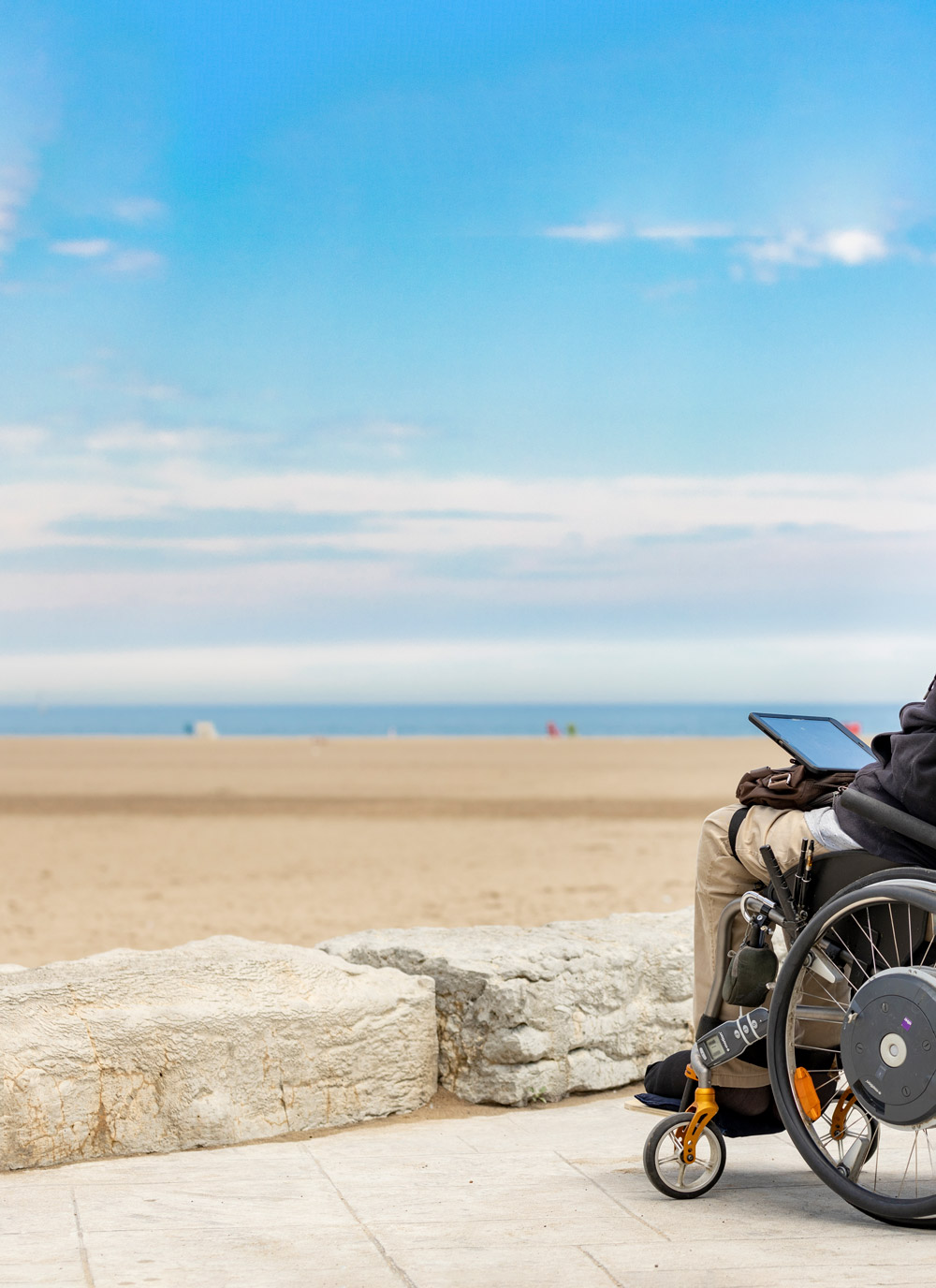 Gentleman in wheelchair holding a tablet by whilst looking at the ocean