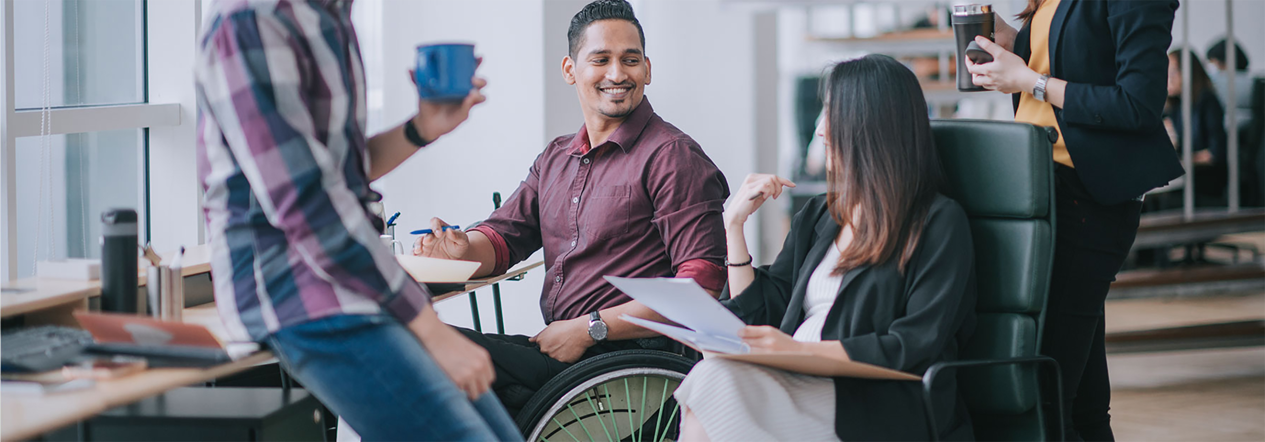 office setting with colleagues casually talking, one worker is in a wheelchair